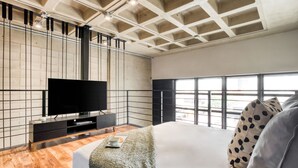 A modern hotel room with a large bed, a flat-screen TV, a wooden floor, and a large window offering a view of the city. - Downtown Loft by ULIV (Tijuana)