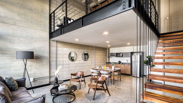 A spacious living area with a high ceiling, a dining table, and a staircase leading to an upper level. - Downtown Loft by ULIV (Tijuana)