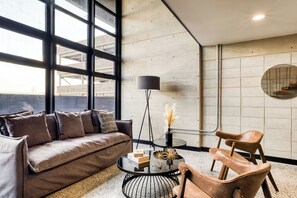 A modern living room with a sofa, coffee table, and chairs, large windows, and a minimalist decor.