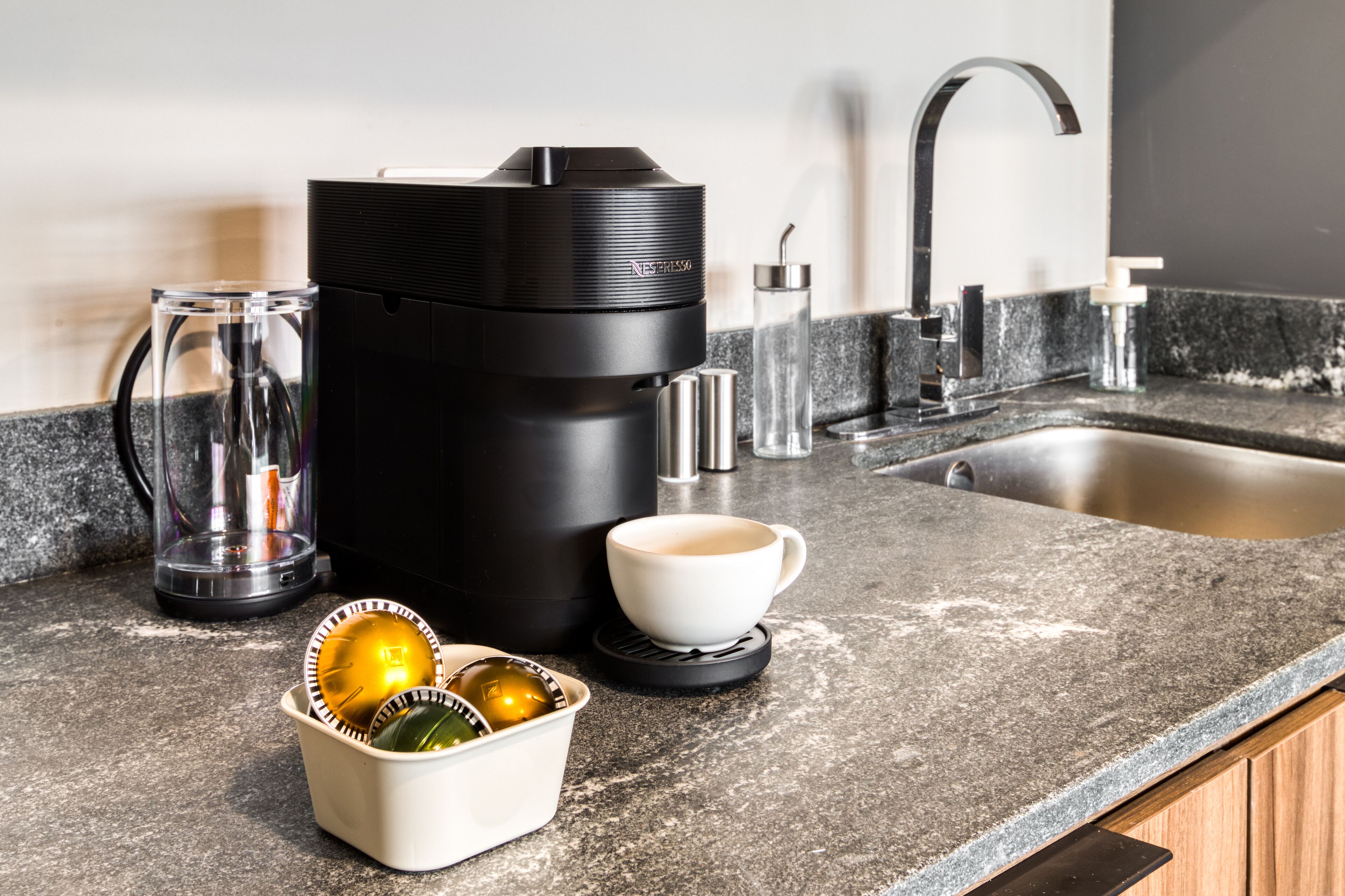 Un piano di lavoro in cucina con una macchina per il caffè, una tazza, una caraffa in vetro e una ciotola con oggetti decorativi.