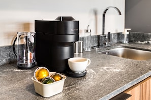 Een keukenblad met een koffiezetapparaat, een kop, een glazen kan en een schaal met decoratieve objecten.