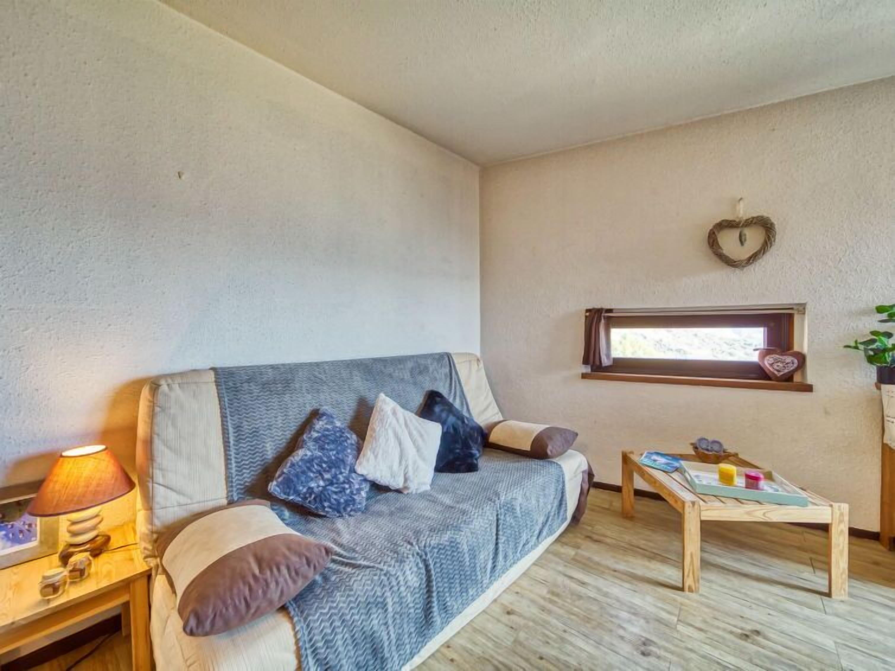 Um quarto aconchegante com um sofá, uma mesinha, um abajur e uma janela com um enfeite em formato de coração.