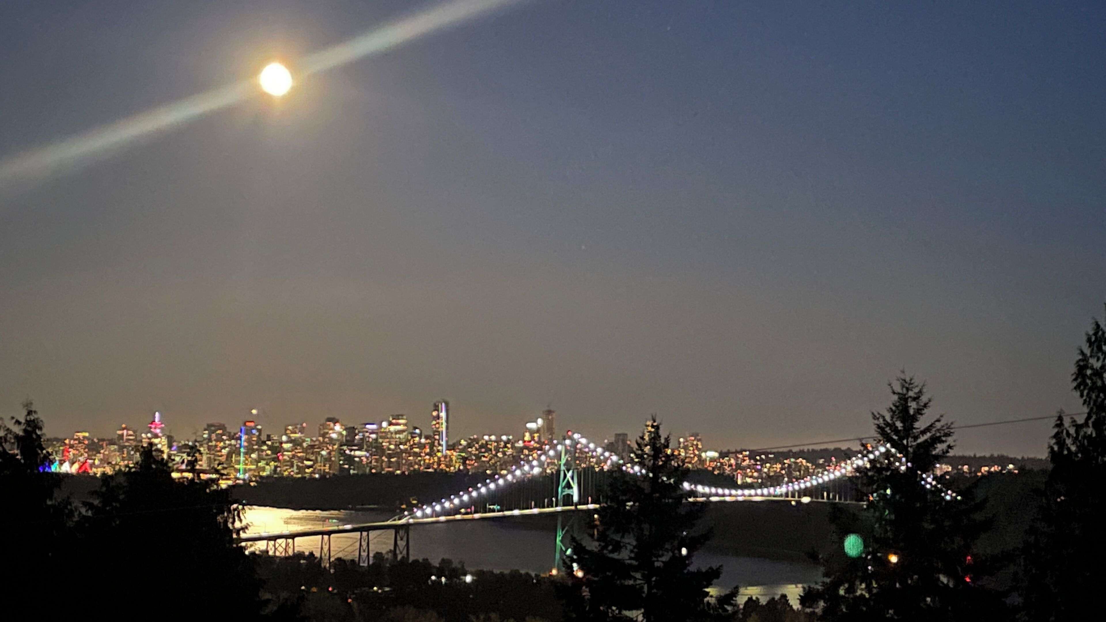 A city skyline at night with a bridge illuminated by lights.