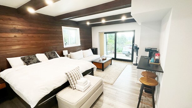 A modern bedroom with a large bed, a small sofa, a coffee table, and a desk with a chair. - 1BR Private Suite · West Vancouver · Landmark View · Prime Location (West Vancouver)