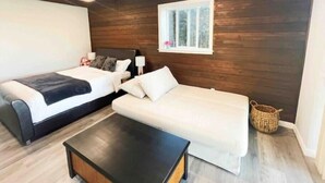 A room with two beds, a sofa, a small table, and a window with a view of trees. - 1BR Private Suite · West Vancouver · Landmark View · Prime Location (West Vancouver)