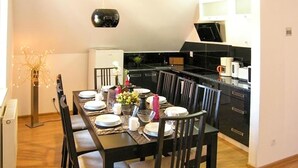 A dining area with a long table set for six, surrounded by chairs. There is a modern kitchen in the background with black cabinets and a white refrigerator. - 3 bedroom pet friendly home in Karpacz (Karpacz)
