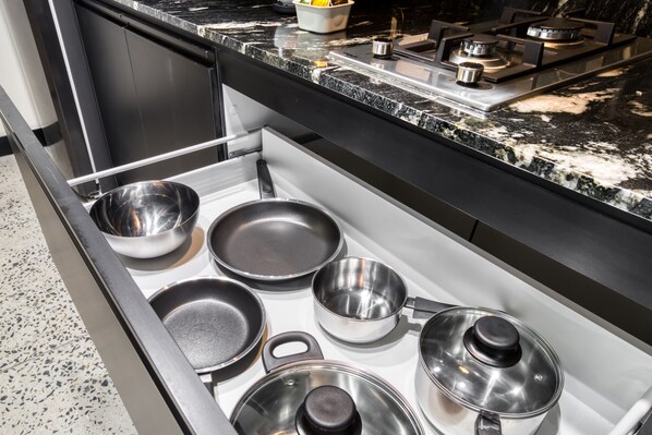 A kitchen drawer with various stainless steel cookware including pots, pans, and lids. - Downtown Designer Apartments by ULIV (Tijuana)