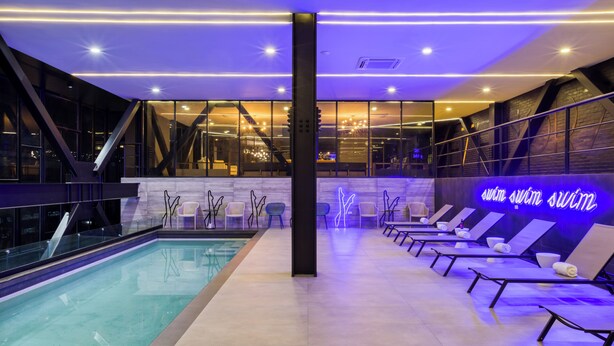 A modern indoor swimming pool area with a neon sign, lounge chairs, and a glass wall. - Downtown Designer Apartments by ULIV (Tijuana)