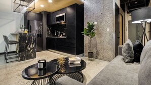 A modern kitchen with black cabinetry, a built-in microwave, and a bar area with stools. - Downtown Designer Apartments by ULIV (Tijuana)