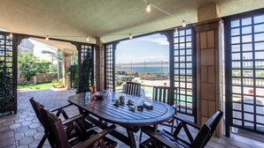 A covered patio with a round table and chairs, a view of the sea, and a stone wall. - Beach front home in Brucoli (Brucoli)