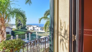 A view from a balcony with a metal railing, overlooking a coastal area with buildings and palm trees. - Beach front home in Brucoli (Brucoli)