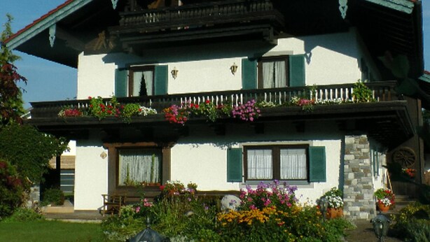 A two-story house with a balcony, a porch with flowers, and a stone staircase.