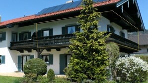 A two-story house with a red-tiled roof, solar panels, and a balcony.