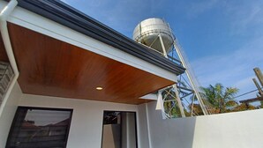 Een modern gebouw met een grote watertank op het dak, een houten uitbouw en een helderblauwe lucht.