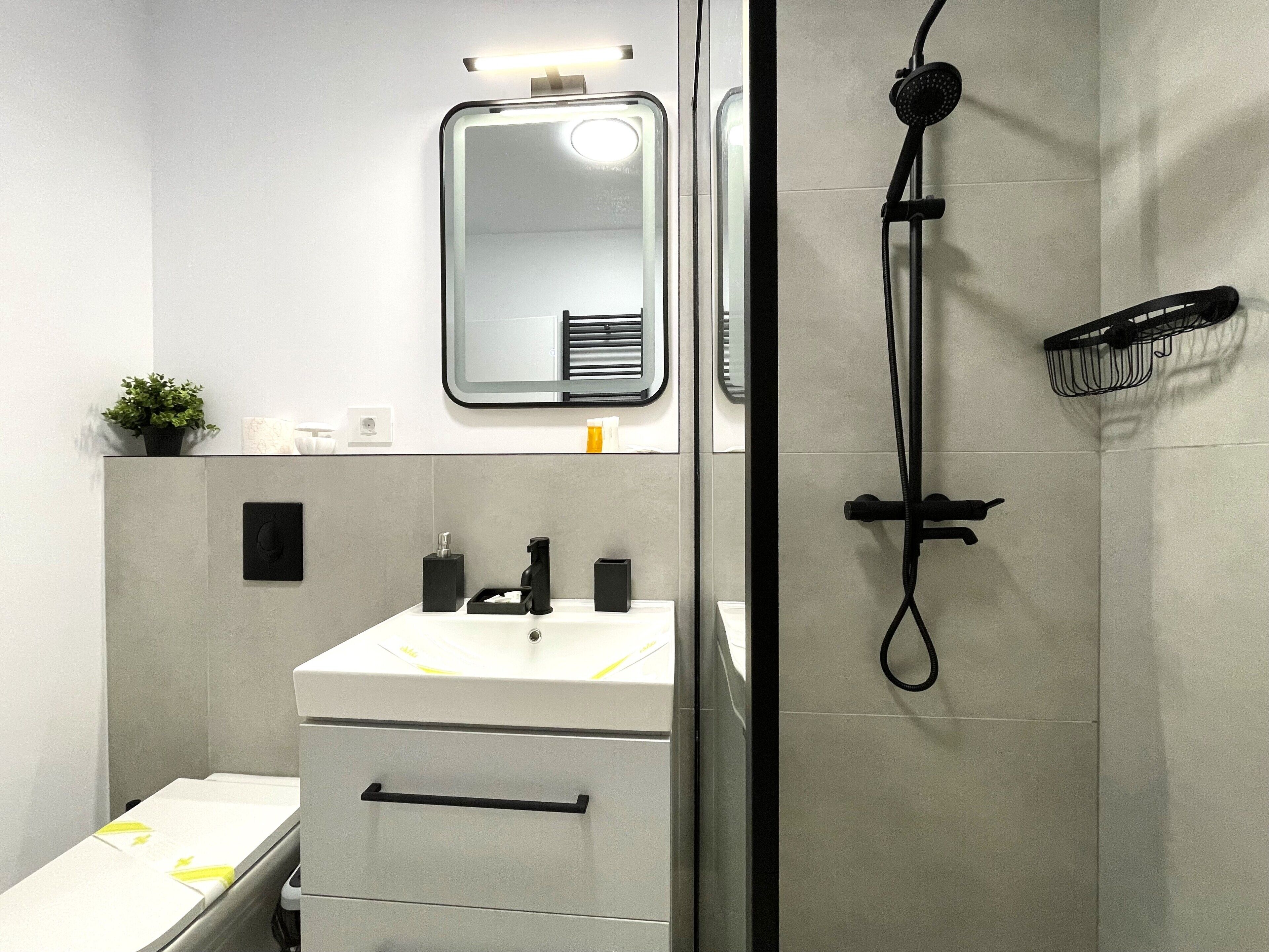 Ein modernes Badezimmer mit einem weißen Waschbecken, einem Spiegel, einer Handbrause und einem Handtuchhalter.
