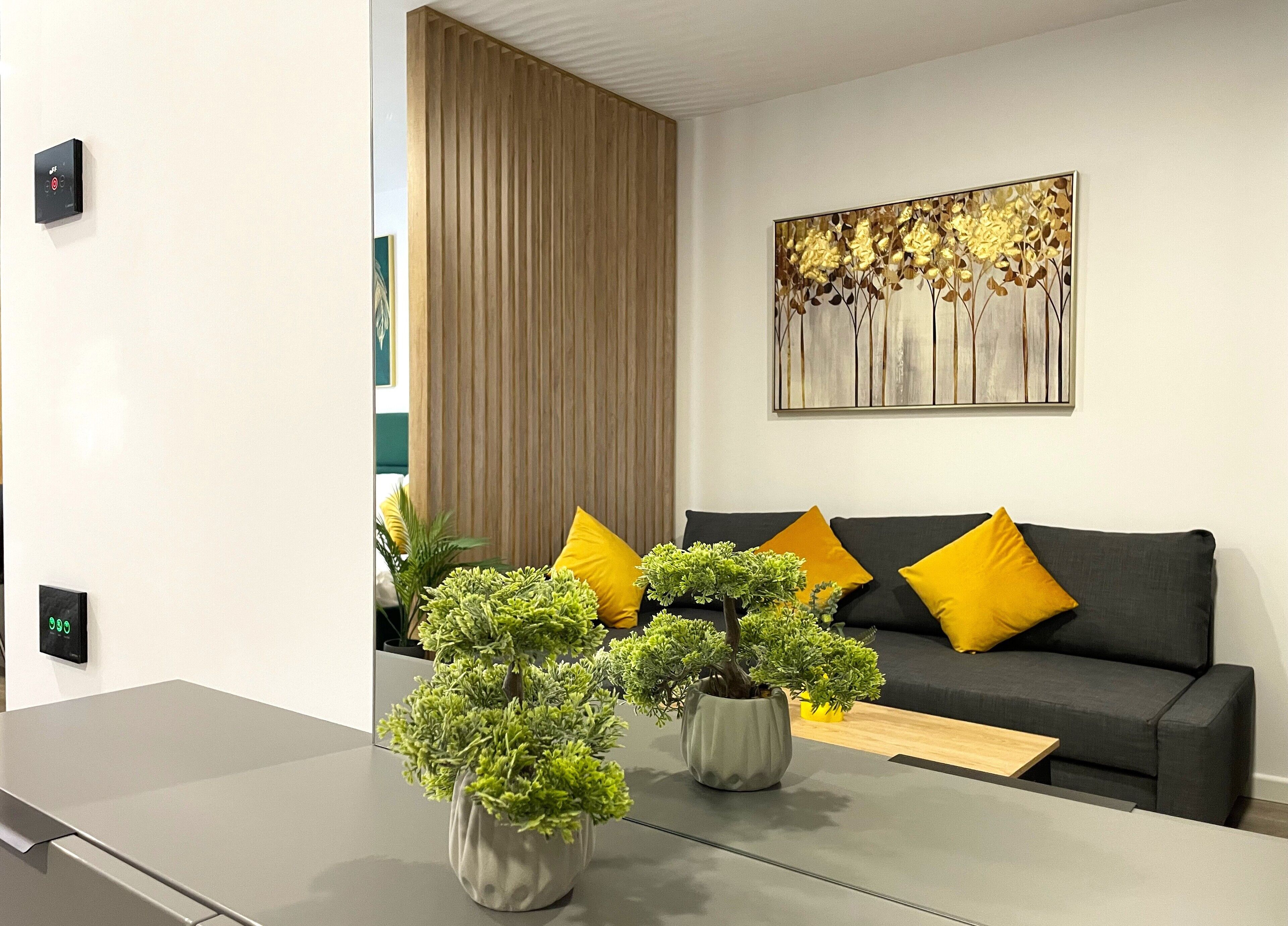 A modern living room with a grey sofa, yellow cushions, and two potted plants.