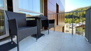 Un balcon doté de meubles en osier, d’une porte vitrée et offrant une vue sur une colline verdoyante.