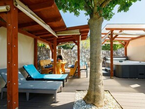 Un espace extérieur abrité, doté de chaises longues, d’un jacuzzi et d’un mur en pierre.