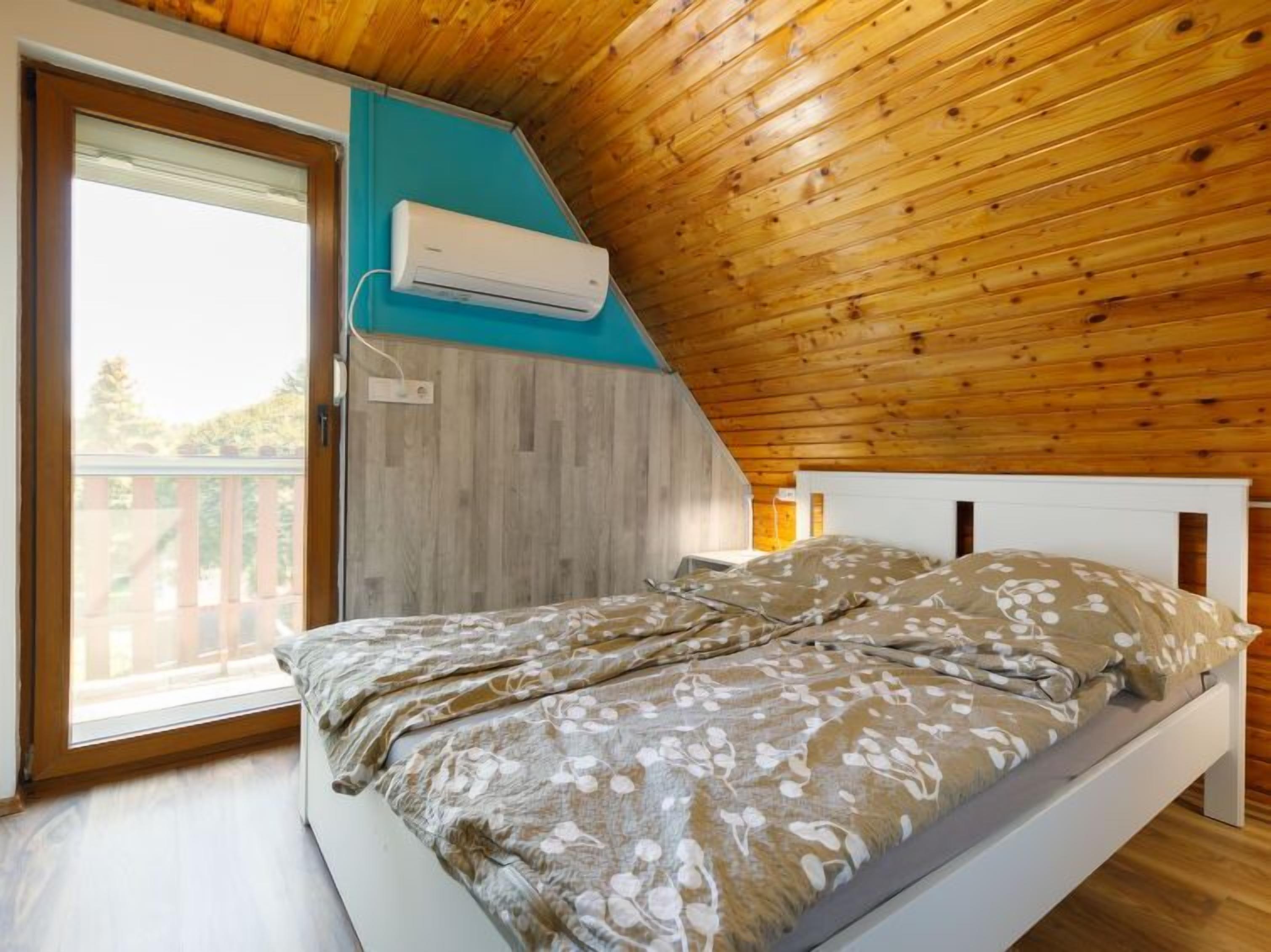 Ein Schlafzimmer mit Holzboden, einem Bett mit floralem Bettzeug, einem Fenster und einer Klimaanlage.