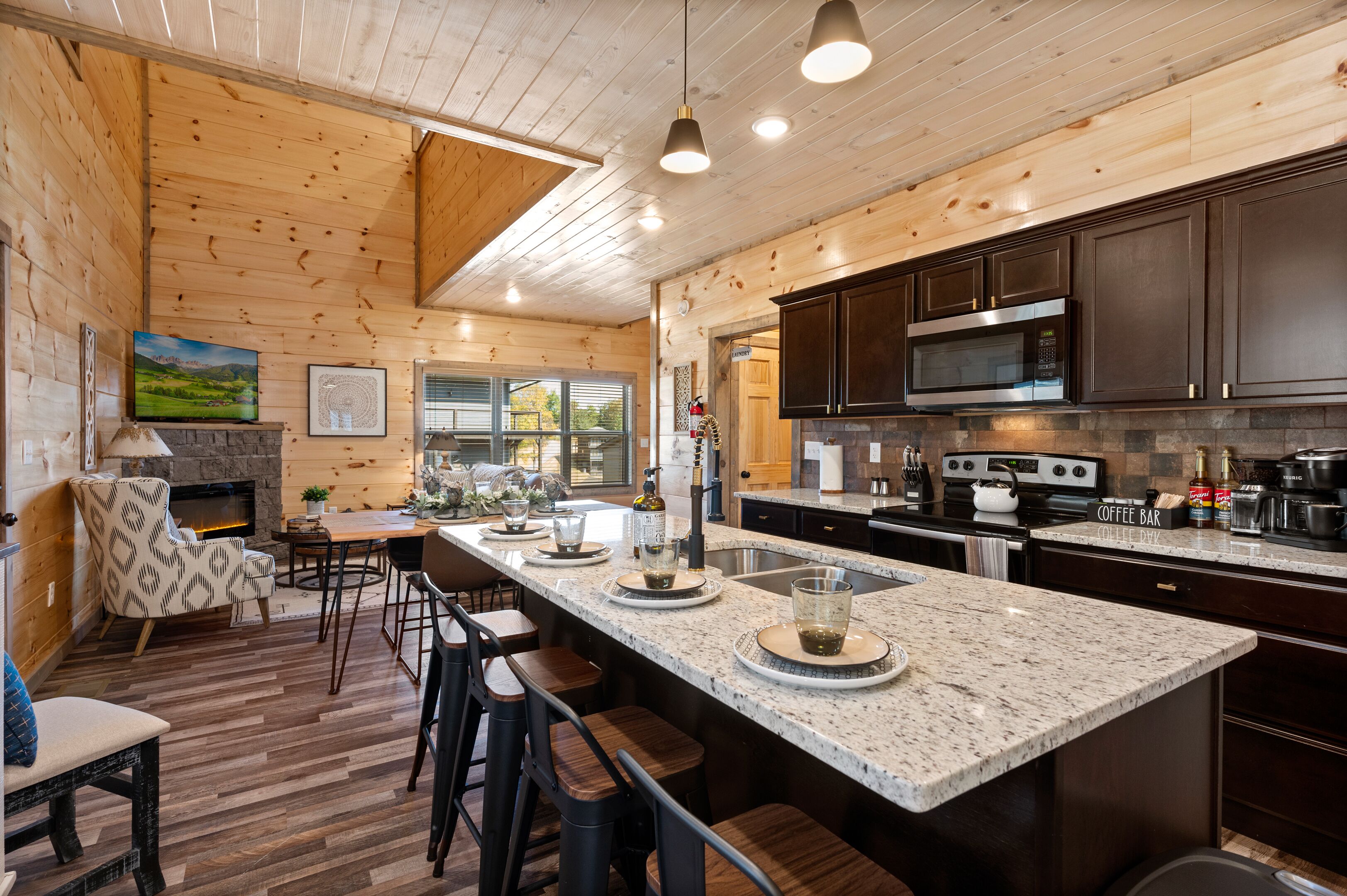 A modern kitchen with a large island, dark cabinets, and a stone fireplace.