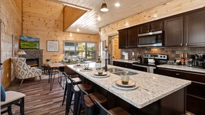 A modern kitchen with a large island, dark cabinets, and a stone fireplace. - SummerFun! Pets, Indoor Pool, Fire Pit, Hot Tub, Foosball/Air Hockey, Dollywood! (Sevierville)