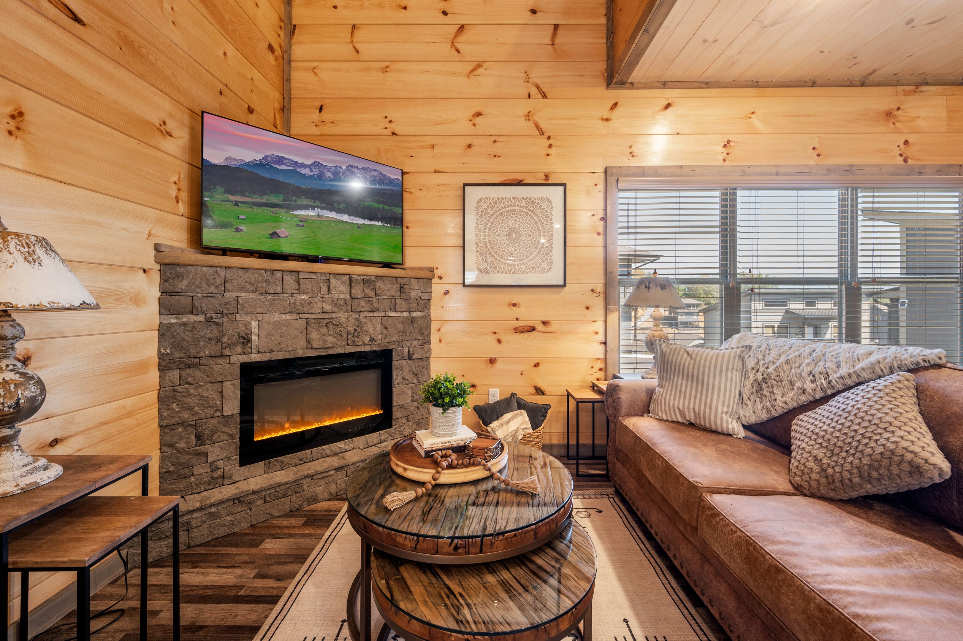 A cozy cabin interior with a stone fireplace, a mounted TV, and a comfortable seating area.