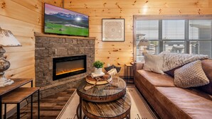 A cozy cabin interior with a stone fireplace, a mounted TV, and a comfortable seating area. - SummerFun! Pets, Indoor Pool, Fire Pit, Hot Tub, Foosball/Air Hockey, Dollywood! (Sevierville)