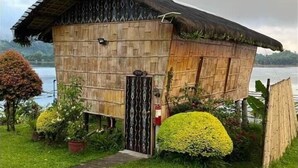 A wooden house with a thatched roof, surrounded by well-maintained greenery and a body of water in the background. - Punta Isla Lake Resort (Lake Sebu)