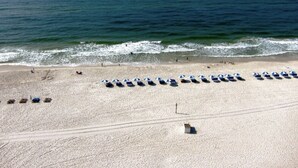 Une plage bordée de rangées de parasols et de chaises longues, un rivage sablonneux et l’océan en toile de fond.