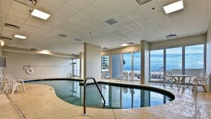 Une piscine intérieure offrant une vue dégagée sur le ciel, ainsi qu’un espace balcon aménagé avec des chaises et des tables.