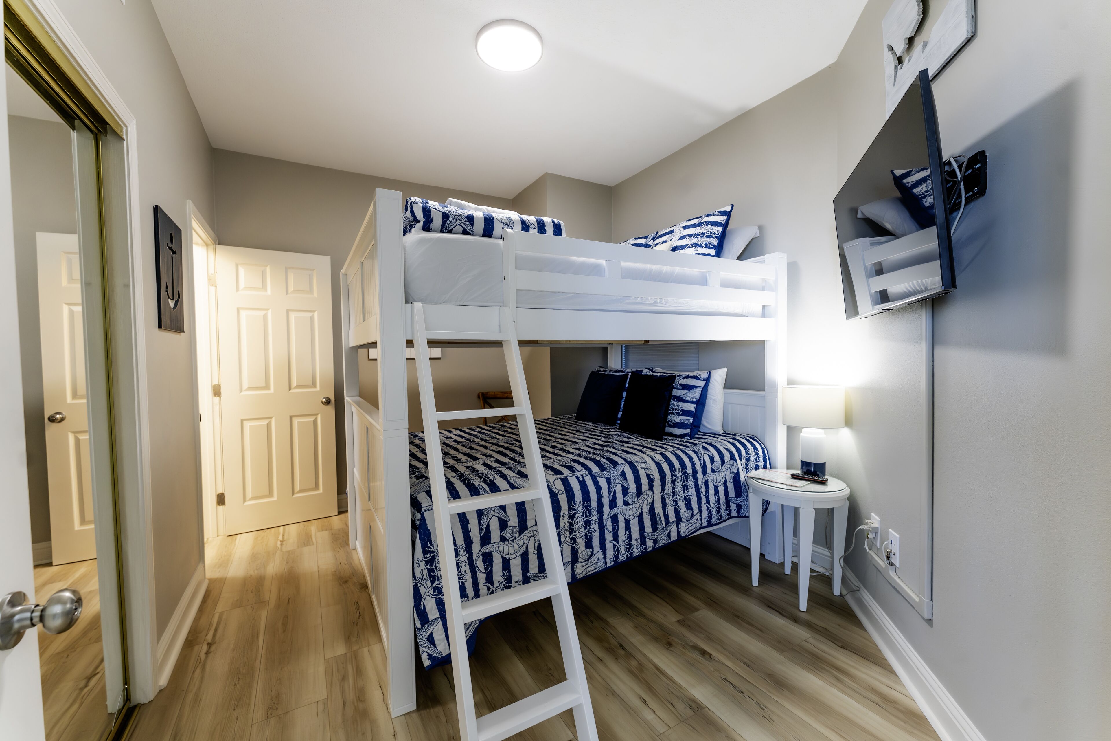 A bunk bed room with a ladder, a small bedside table, and a wall-mounted TV.
