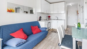 Ett modernt kök med vita skåp, en matplats med ett glasbord och en blå soffa med röda kuddar.