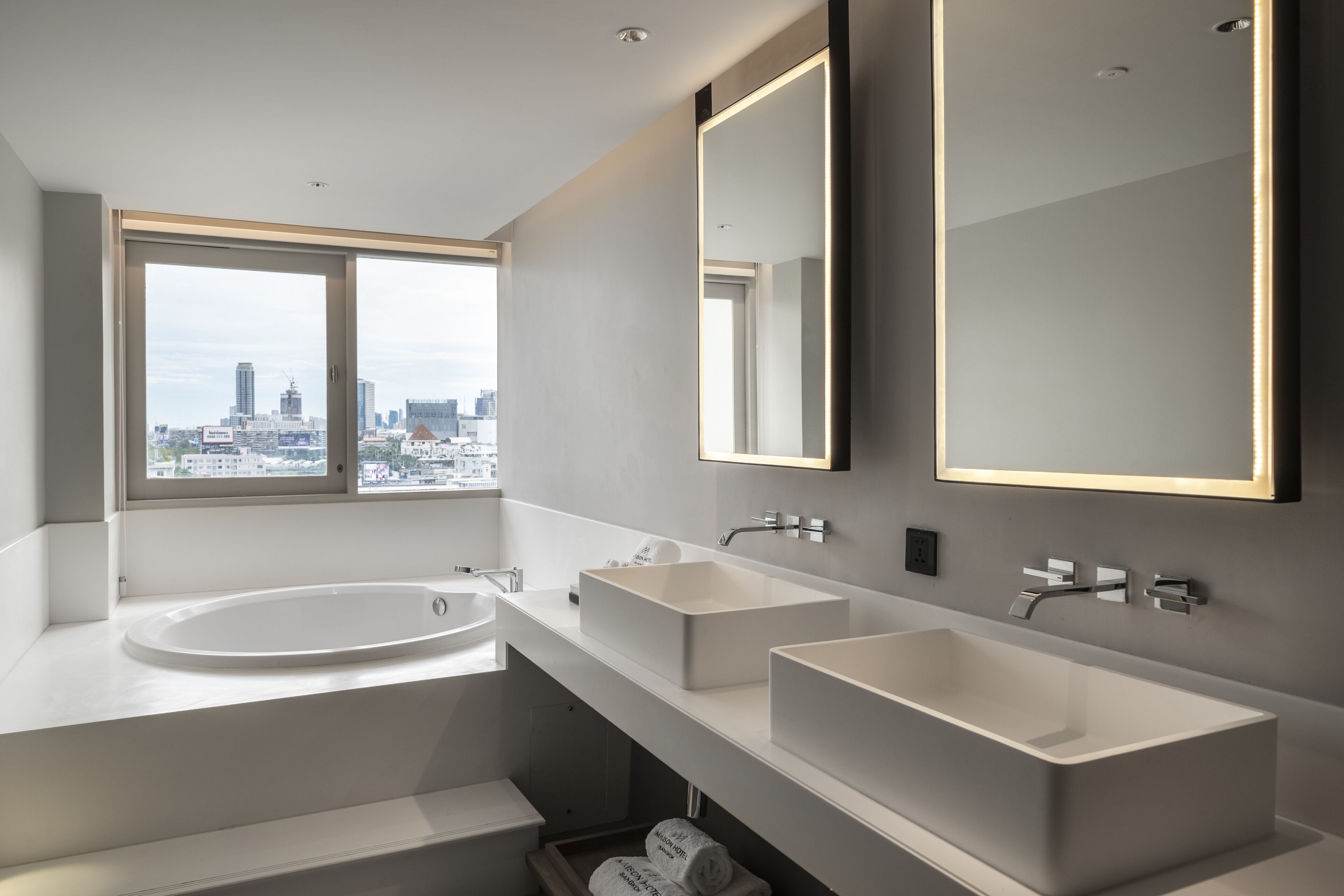 A modern bathroom with a large window, two sinks, and a bathtub.