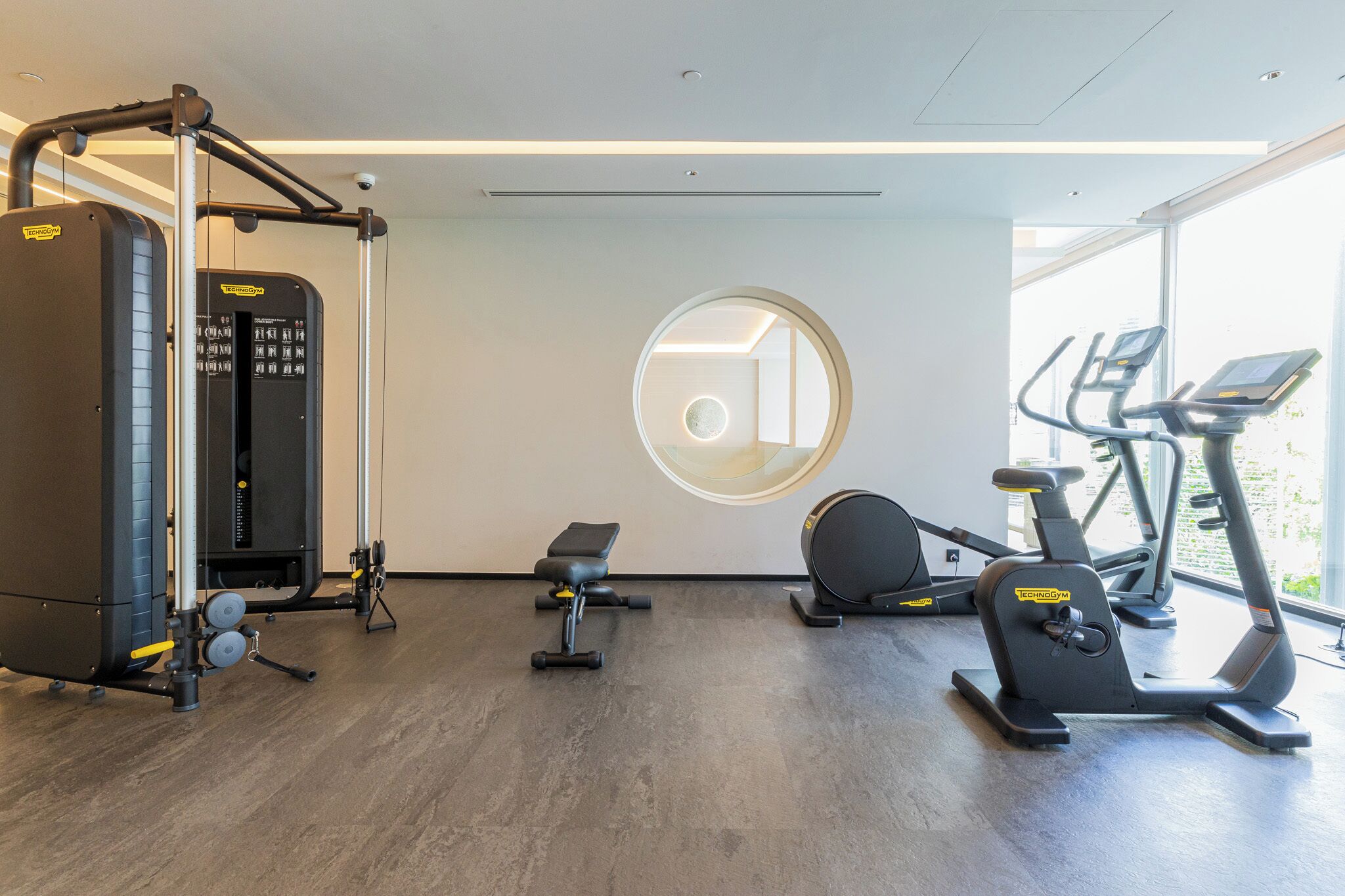 Un gimnasio moderno con equipamiento cardiovascular, máquinas de pesas y un banco.