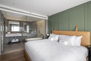 Una habitación de hotel moderna con una cama grande, cabina de ducha con vidrio y una pared verde de acento.