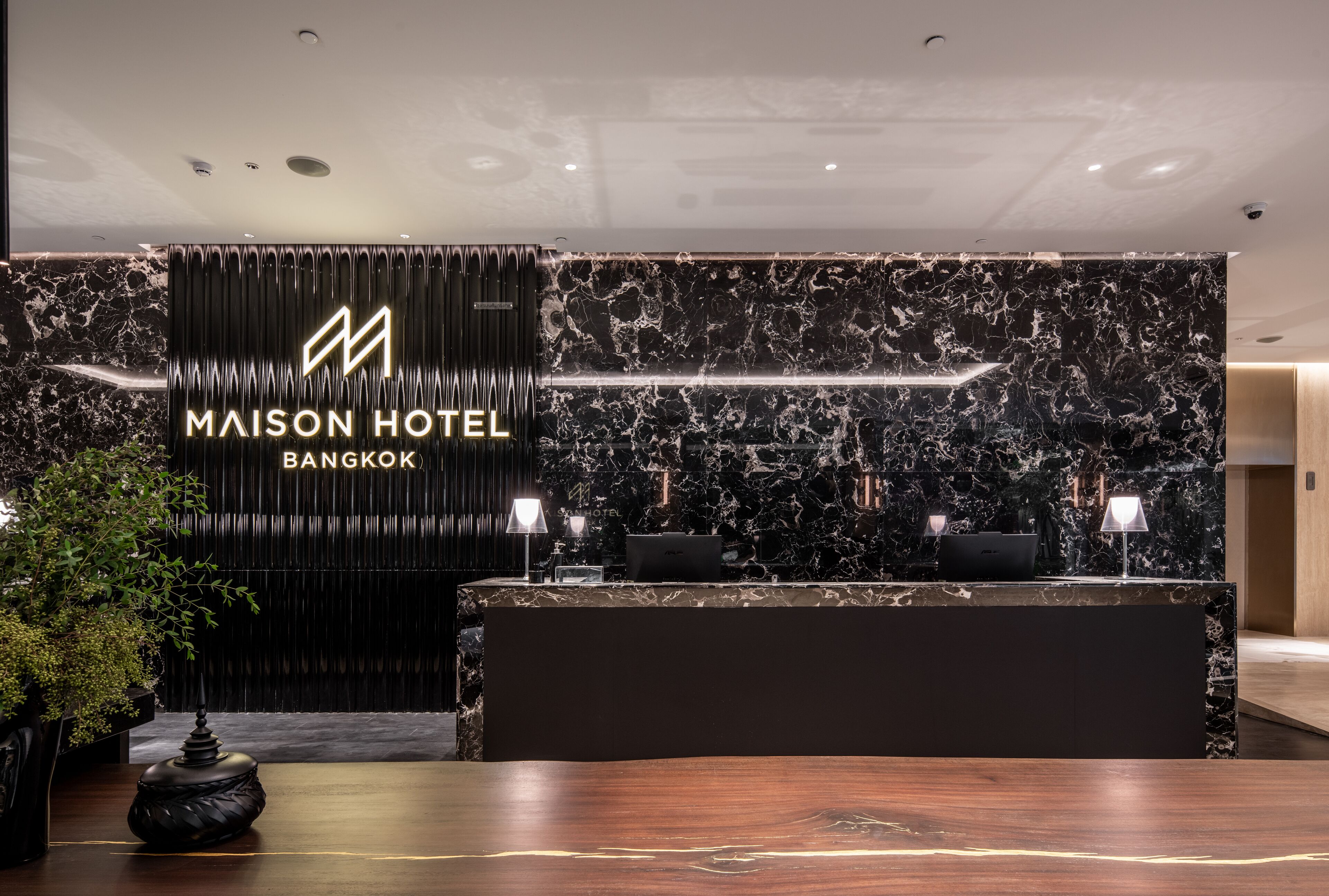 En moderne receptionsdisk med baggrund i marmor, et logo og navnet 'MAISON HOTEL BANGKOK'.