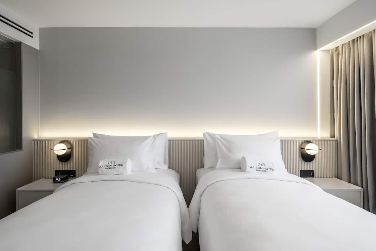 Une chambre d’hôtel avec deux lits, une table de chevet avec une horloge et un luminaire fixé au mur.