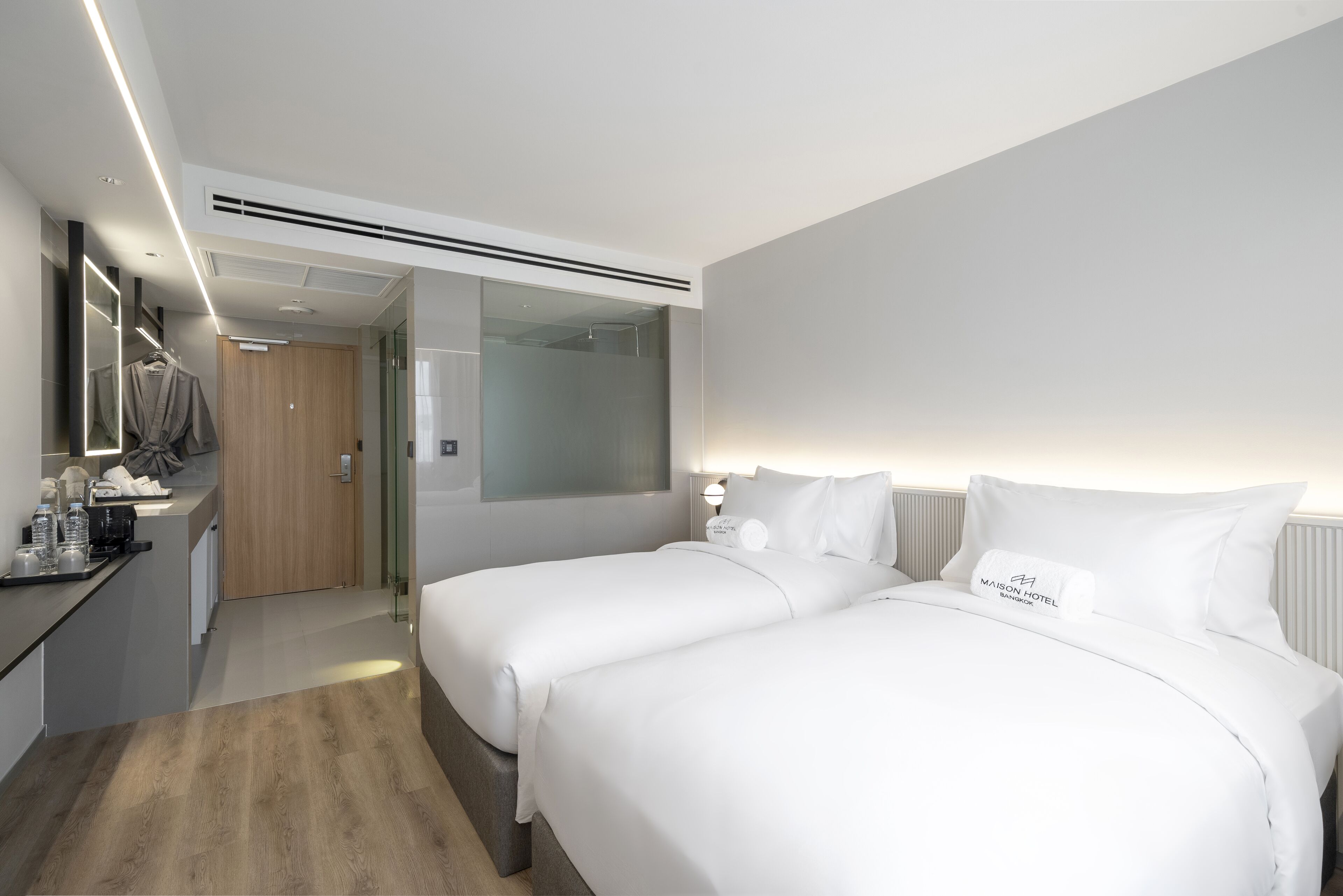 Una habitación de hotel moderna con dos camas, un armario de madera, un espejo y una pequeña kitchenette.