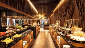 Un espace buffet comprenant différents postes de service pour les aliments, un comptoir central où les plats sont présentés, et un long comptoir avec des assiettes et des bols.