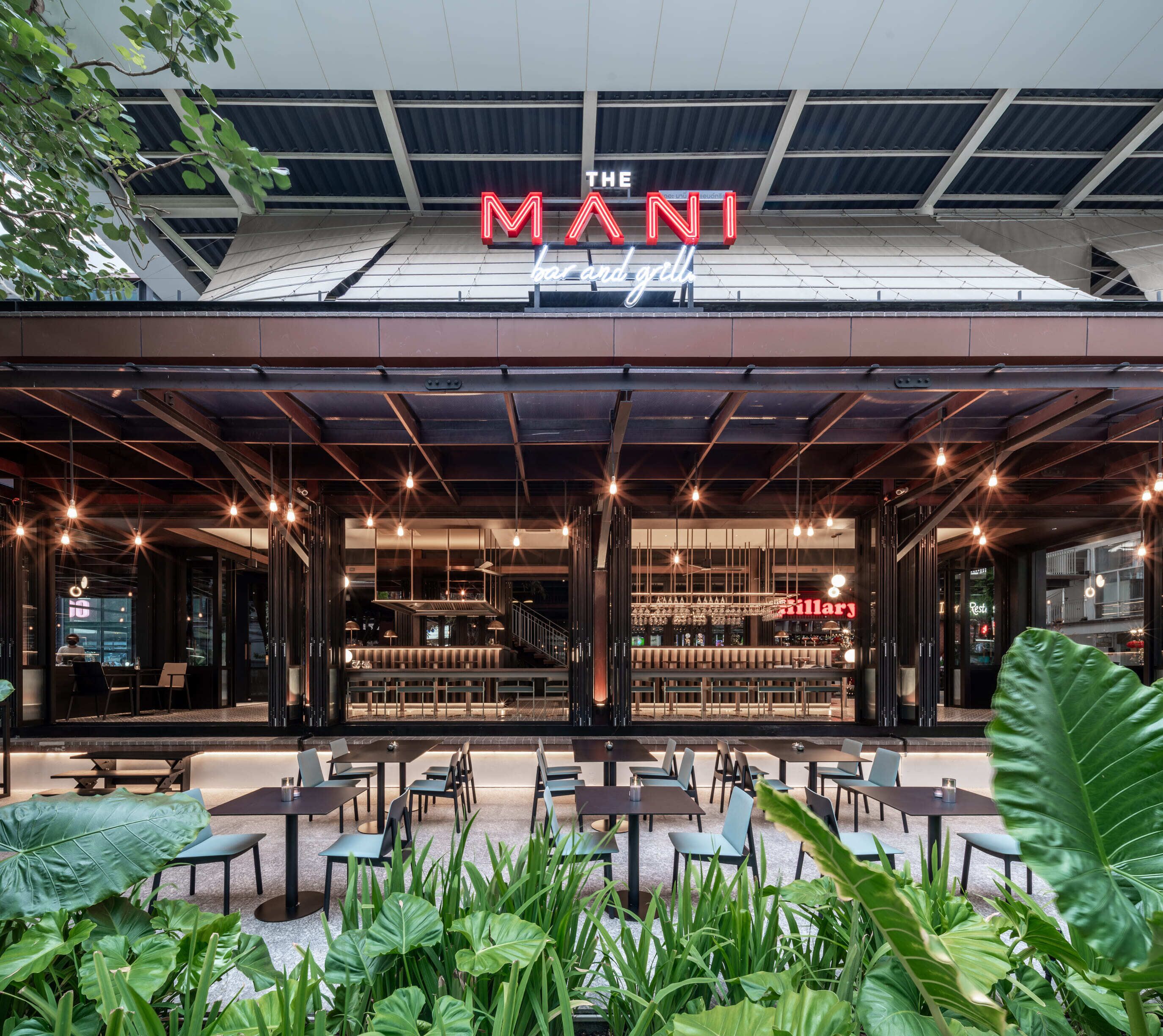 A modern restaurant with a neon sign, outdoor seating, and a staircase leading to an upper level.