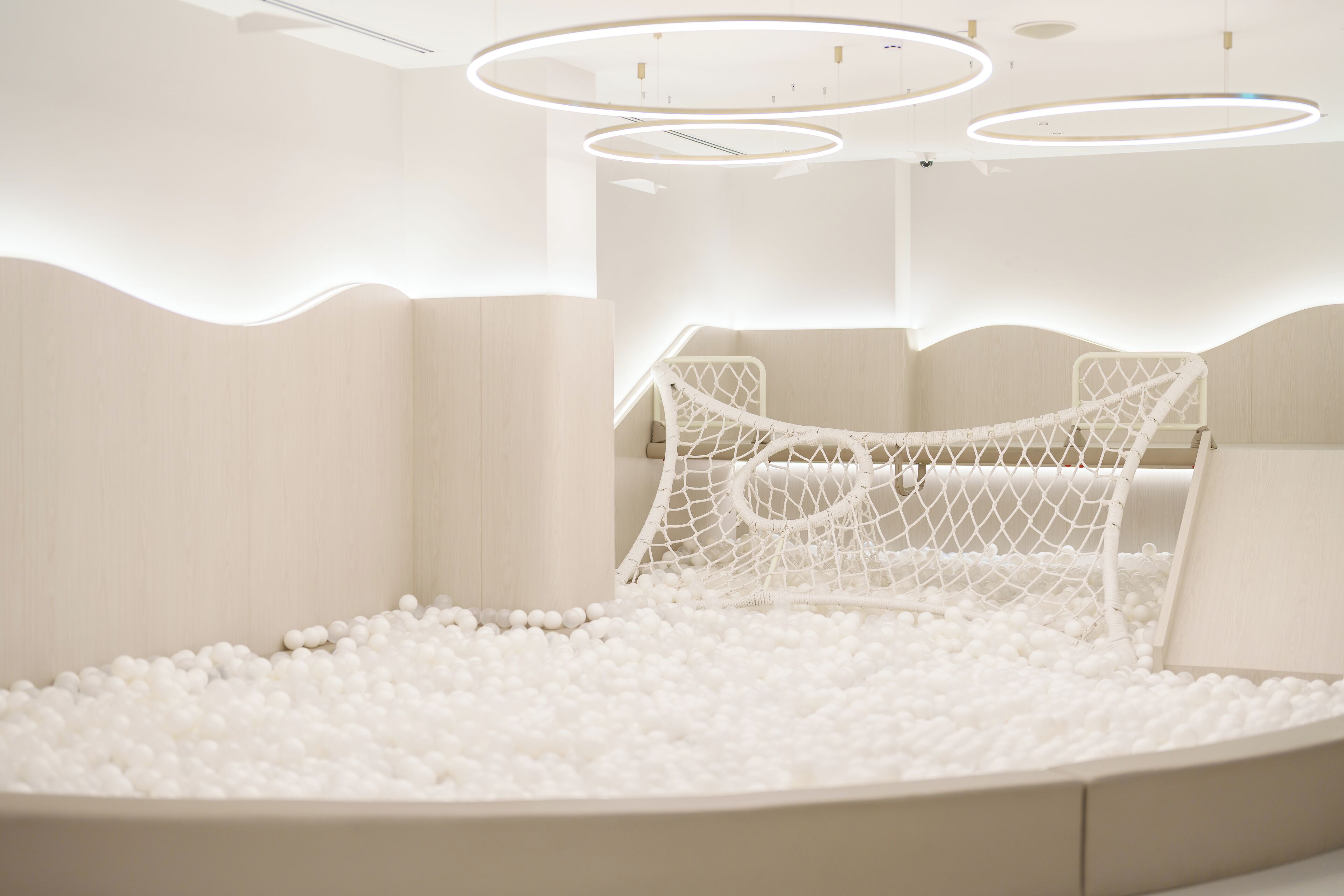 A modern, minimalist room with a white ball pit, a hammock, and a bed with a white headboard.