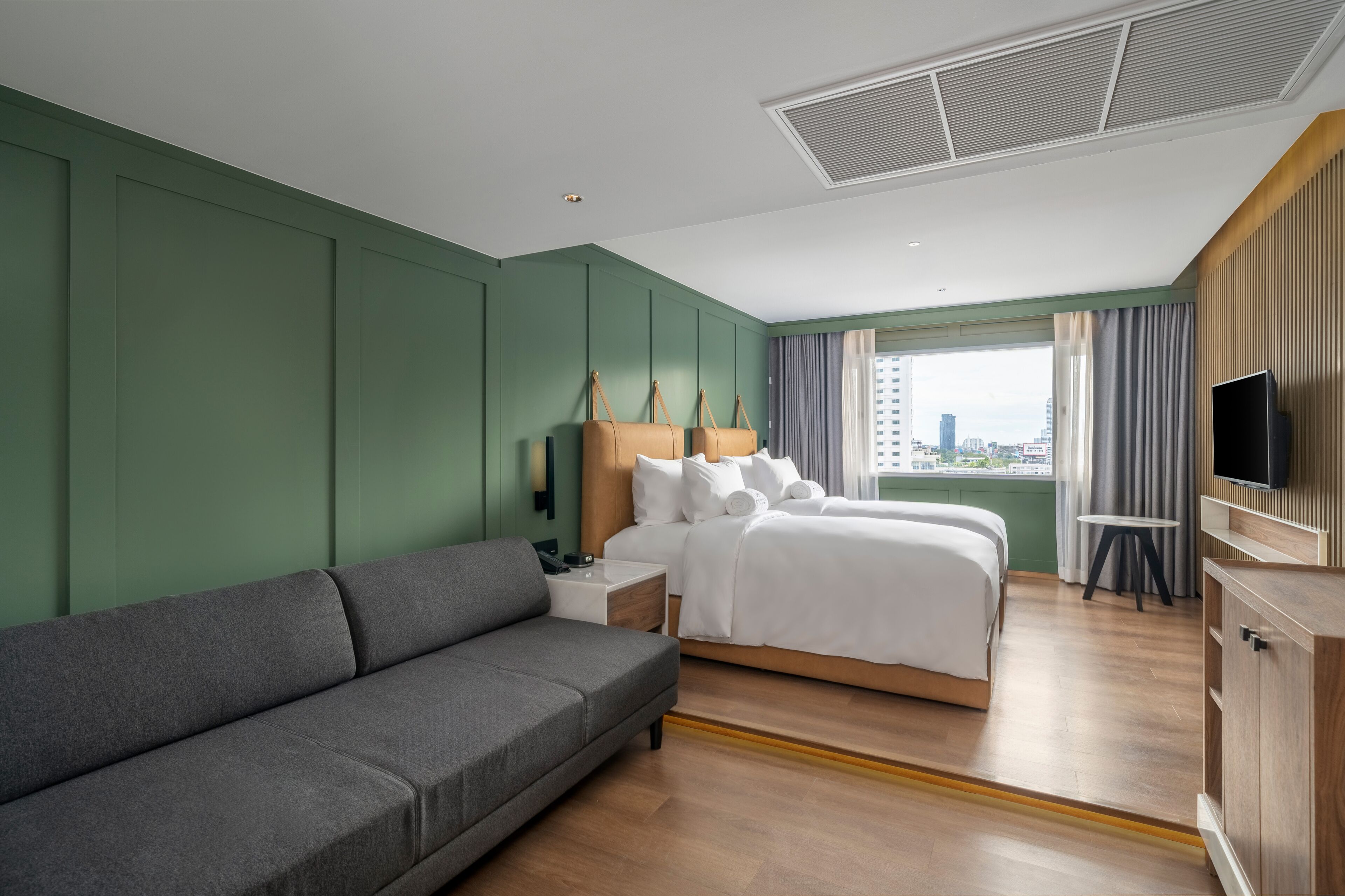 A hotel room with a large bed, a sofa, a TV, and a city view.