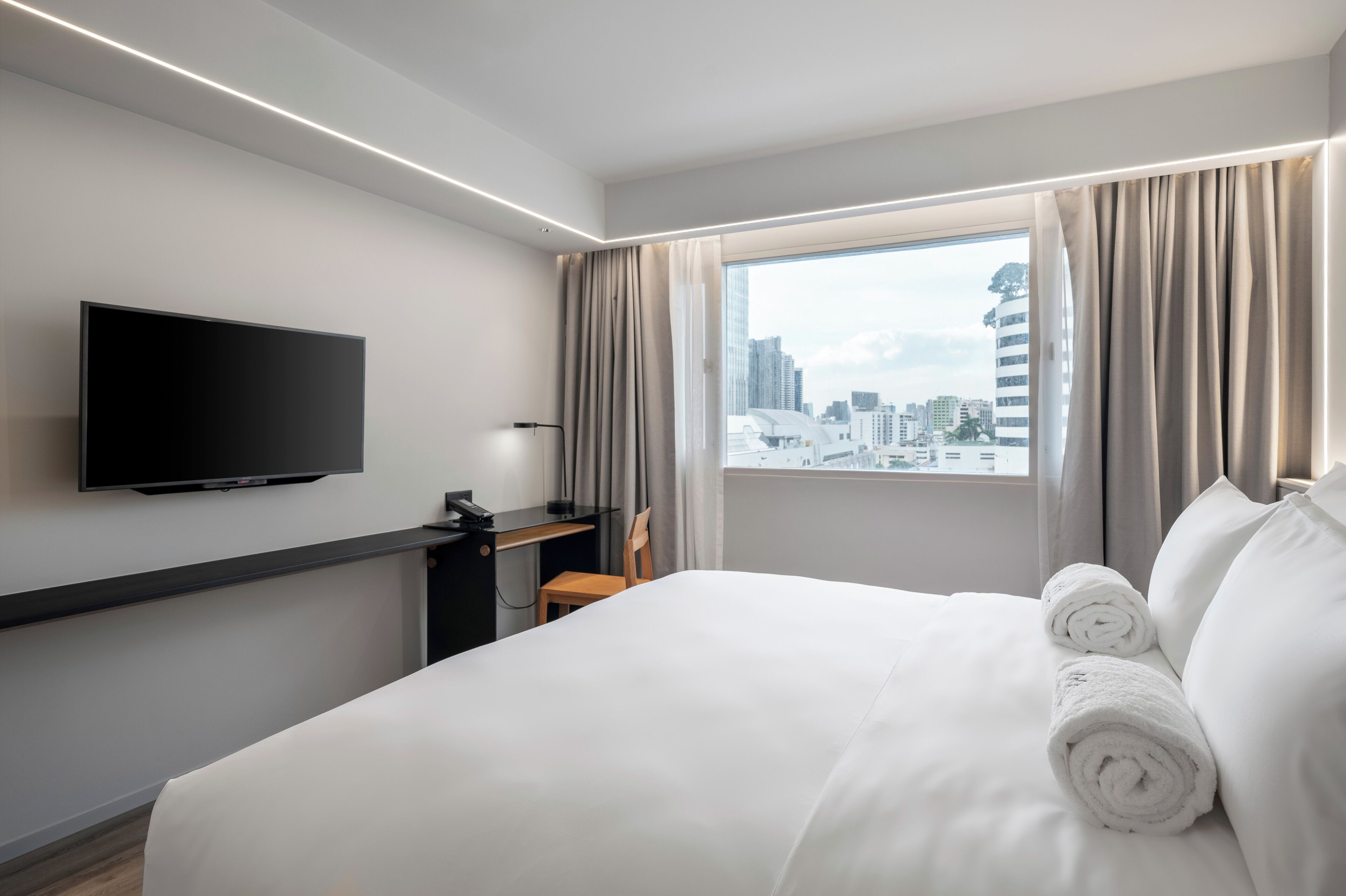 A hotel room with a bed, a desk, a chair, a TV, and a window with curtains.