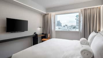 A hotel room with a bed, a desk, a chair, a TV, and a window with curtains.