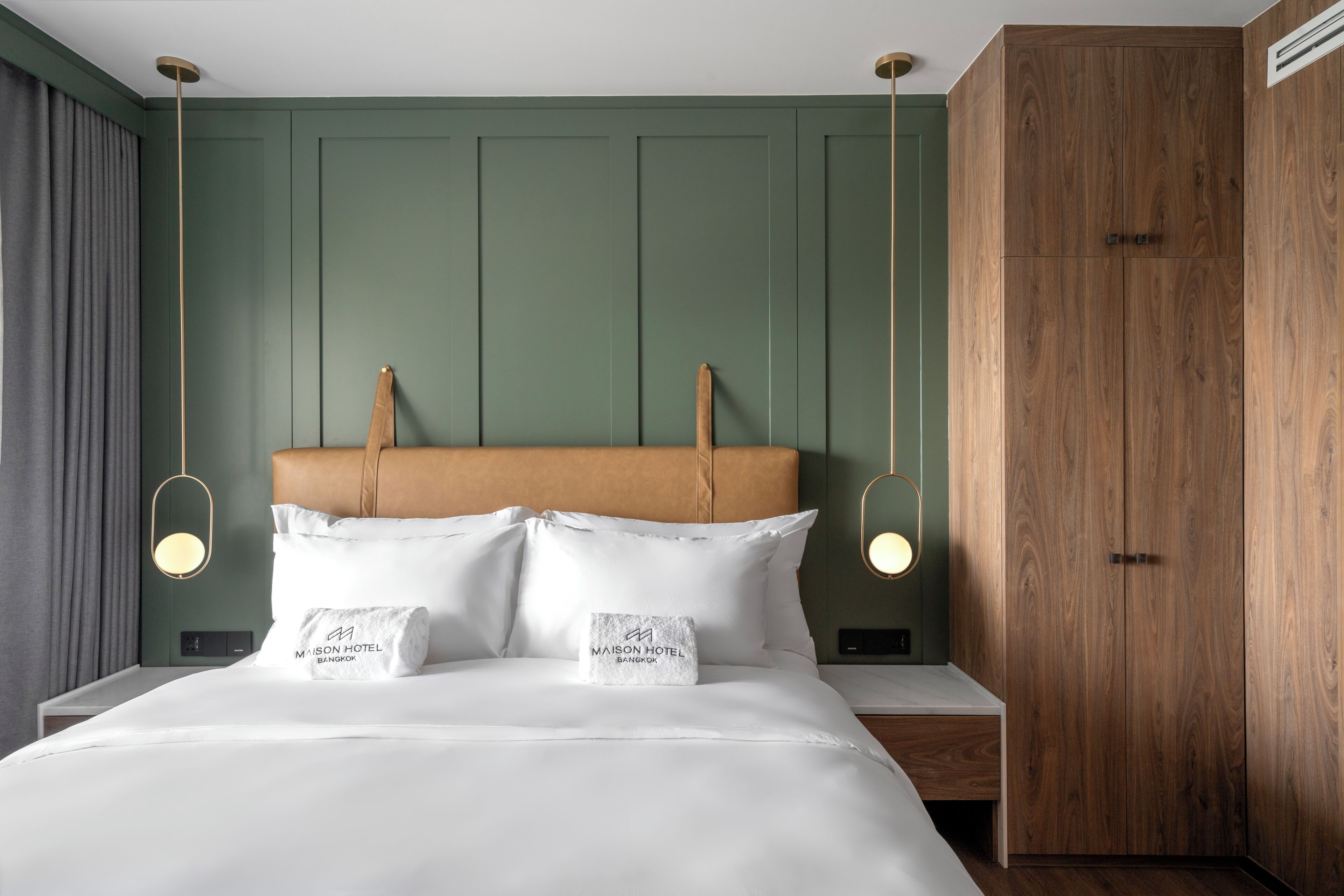 Habitación de hotel con cama, mesitas de noche, armario de madera e iluminación colgante.