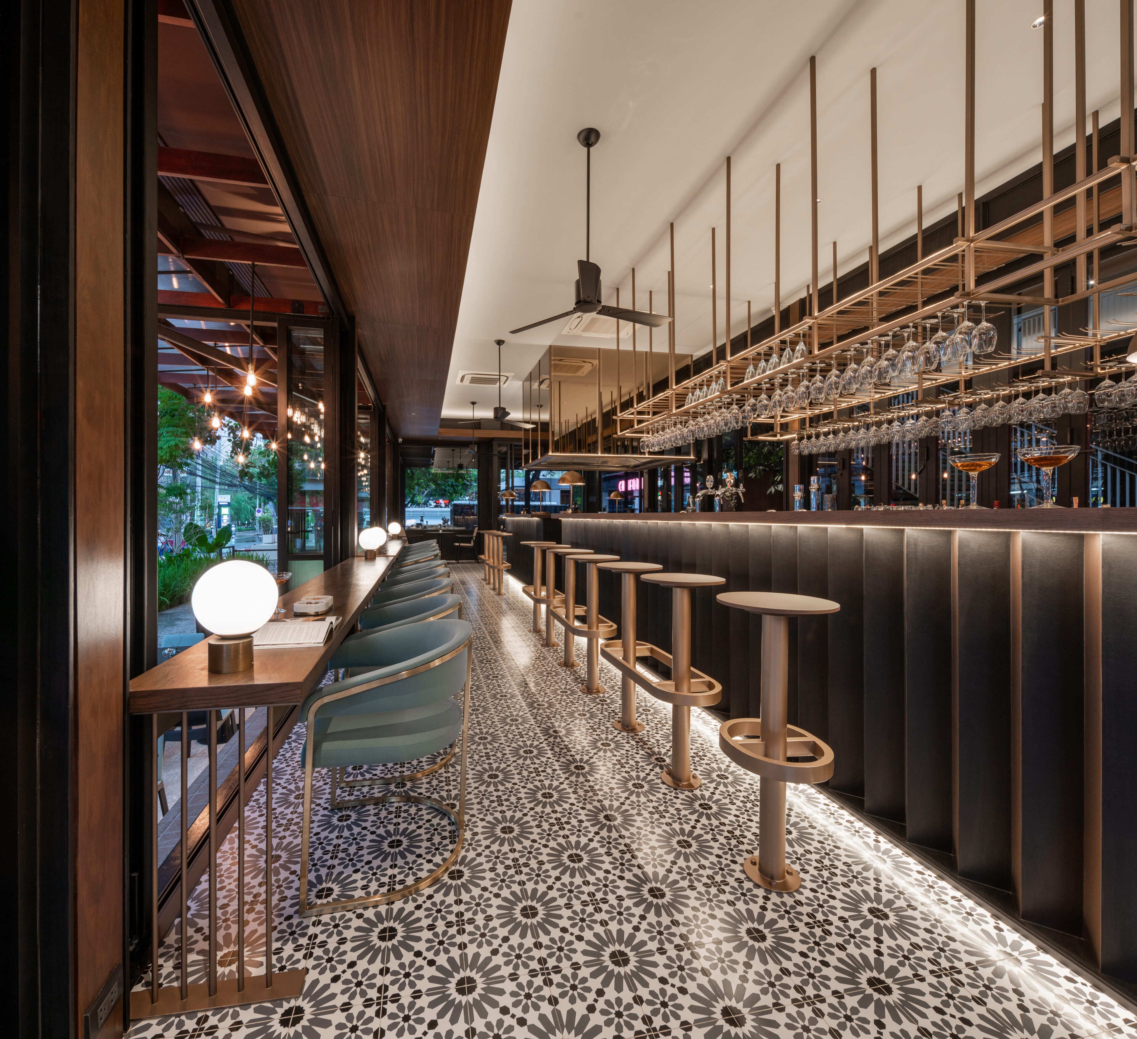 Un espace bar moderne avec un long comptoir, des tabourets et des verres suspendus.