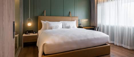 A modern hotel room with a large bed, wooden headboard, bedside tables, and a view of the city through sheer curtains.