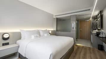 A modern hotel room with a large bed, bedside tables, a vanity with a mirror, and a walk-in closet.