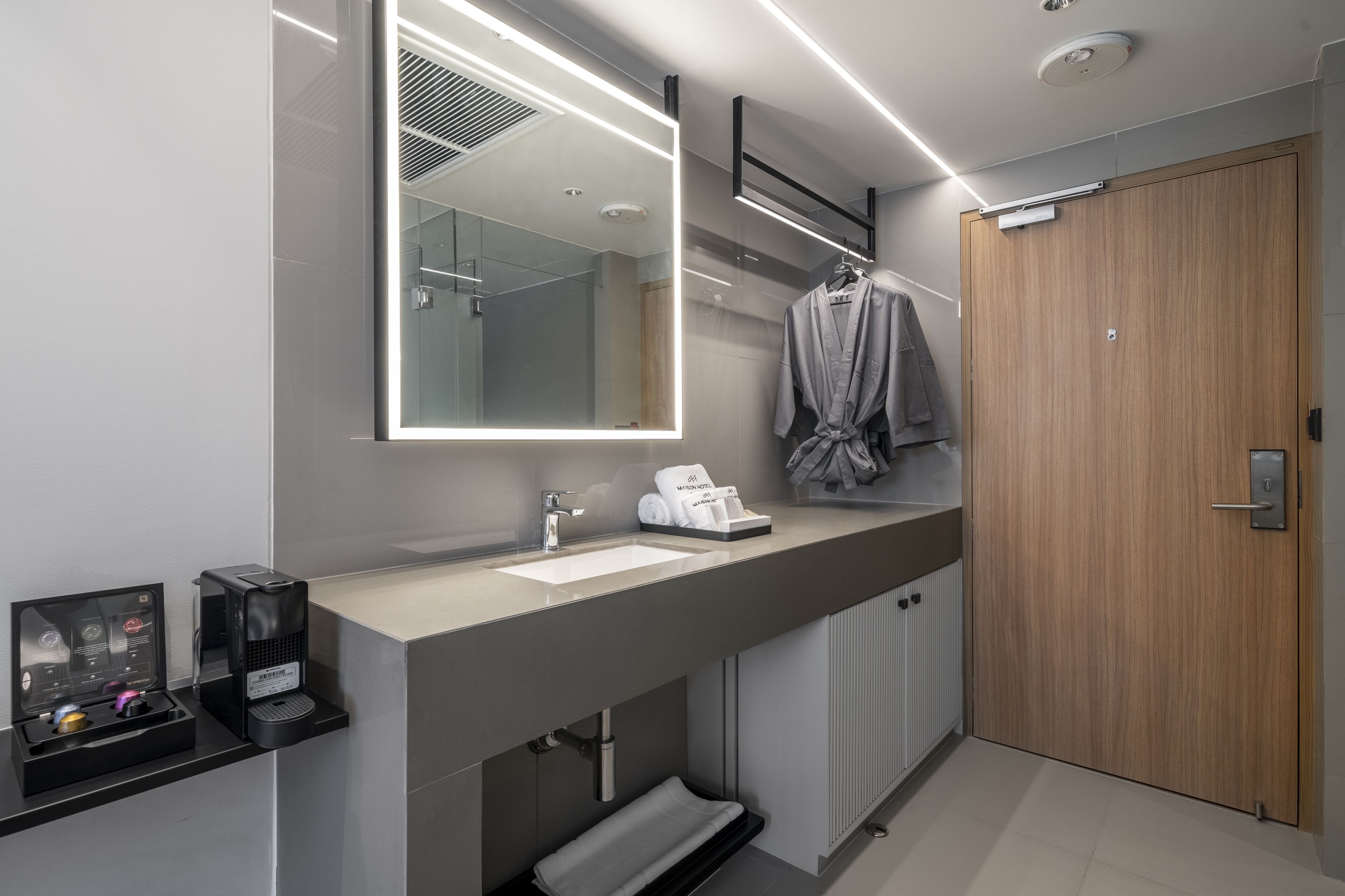 A modern bathroom with a large mirror, a sink, a towel rack, and a wooden door.