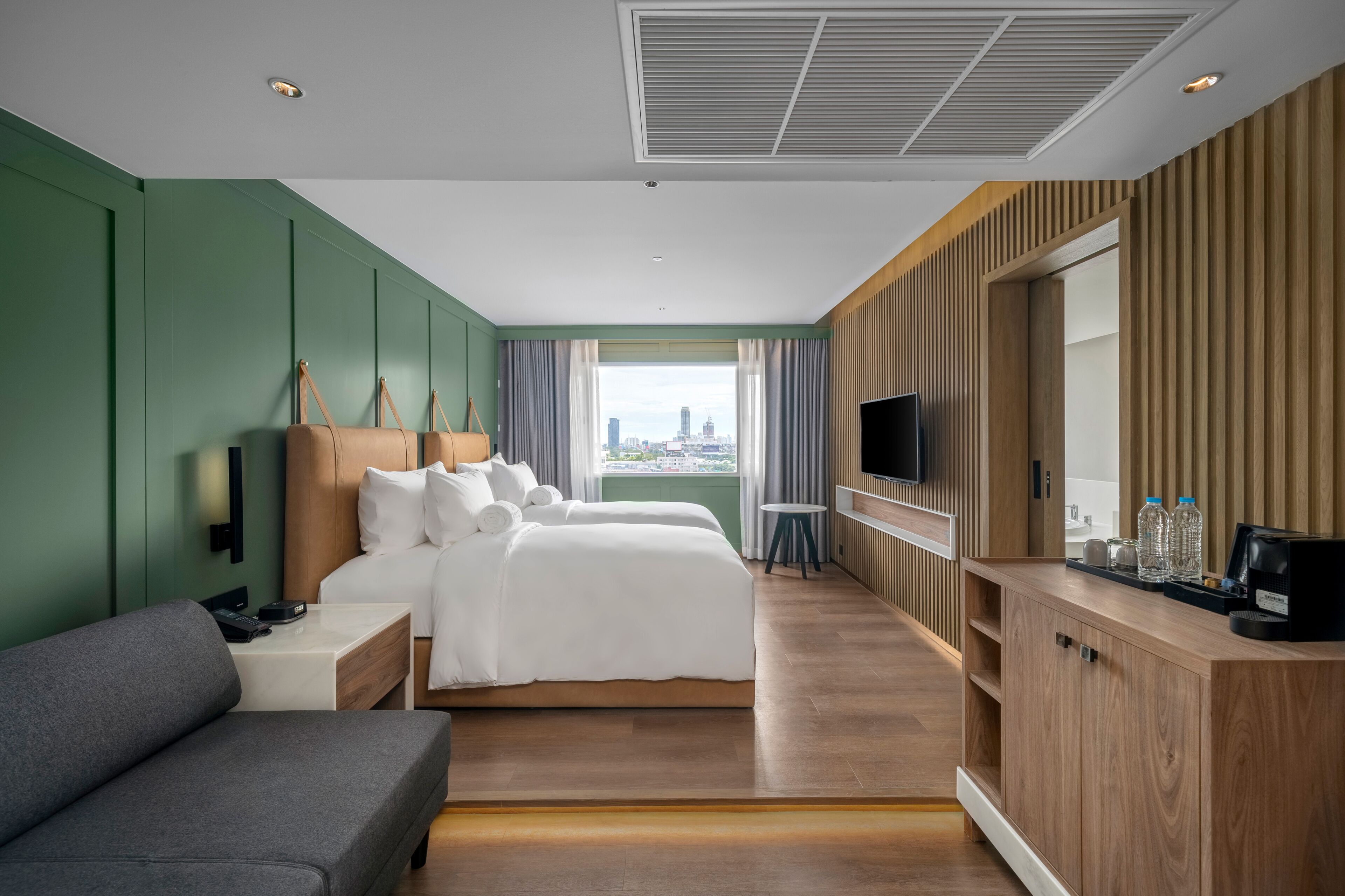 A hotel room with two beds, a sofa, a TV, and a city view.